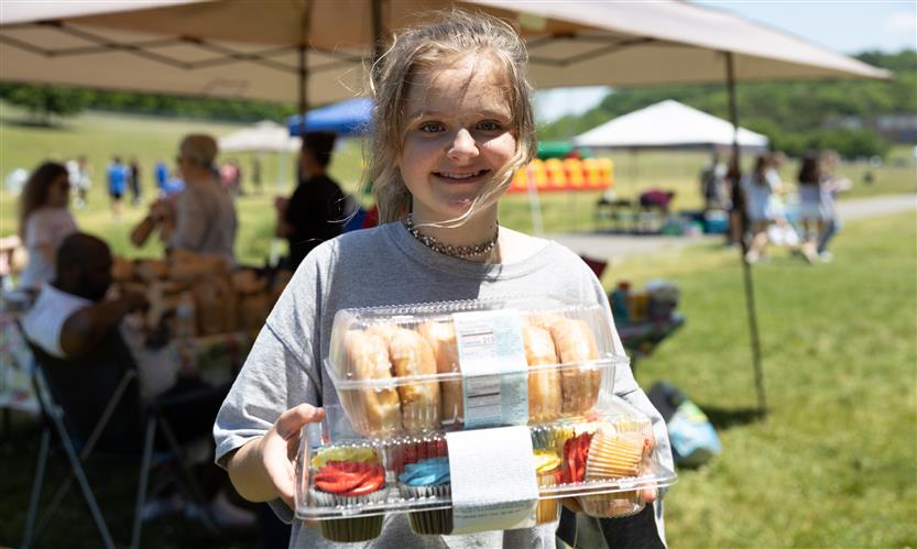 A girl holds a box of donuts and a box of cupcakes